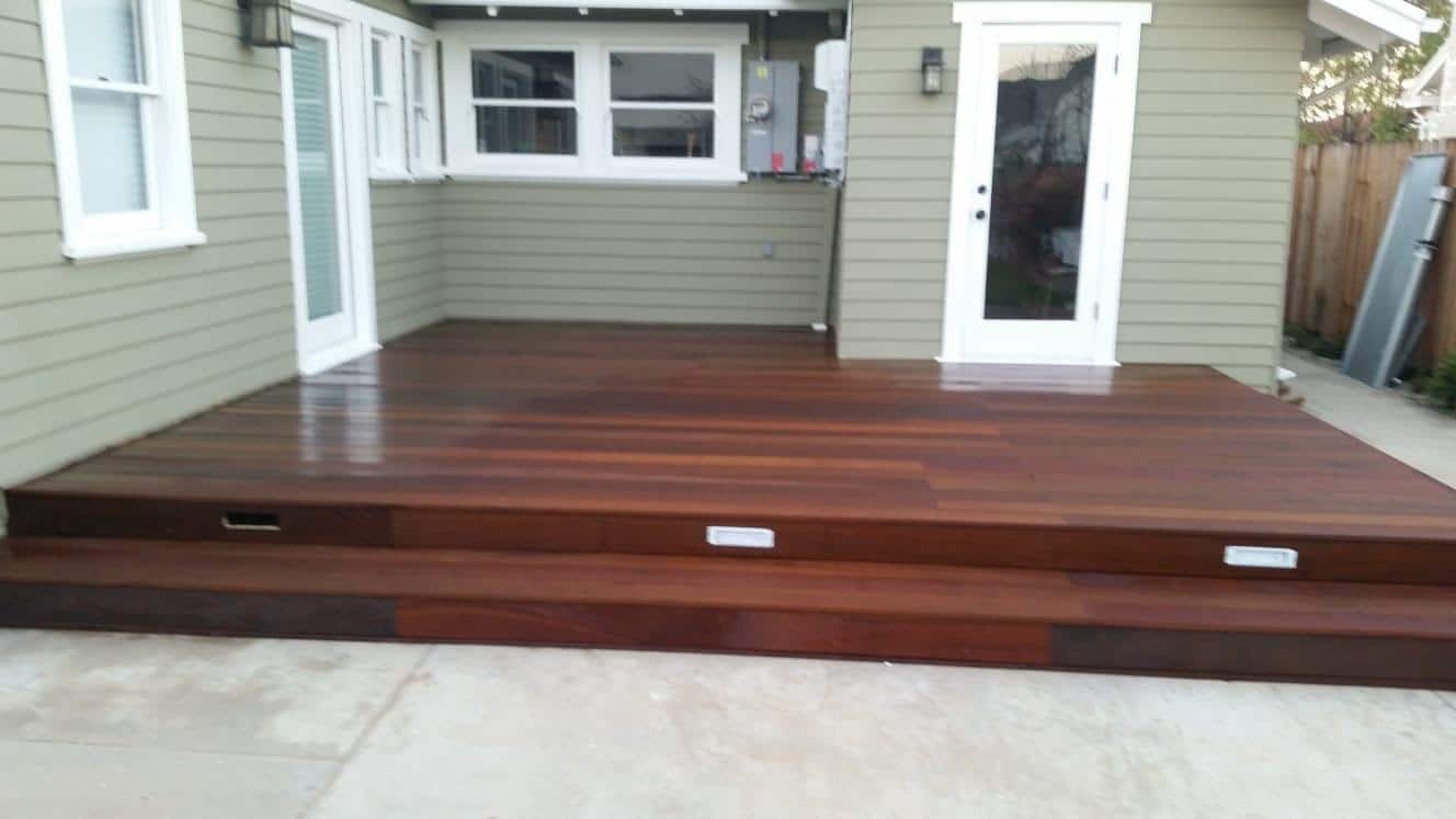 New dark-stained hardwood deck with two-tier steps and recessed step lights against green house exterior.