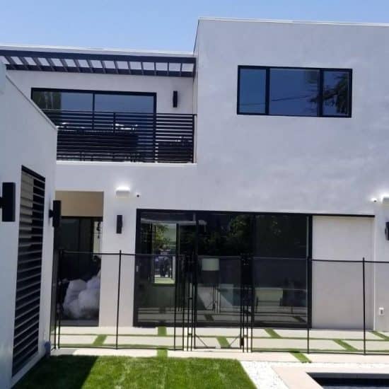 Modern two-story white stucco house with large sliding glass doors, second-floor balcony, pool fence, and manicured lawn.
