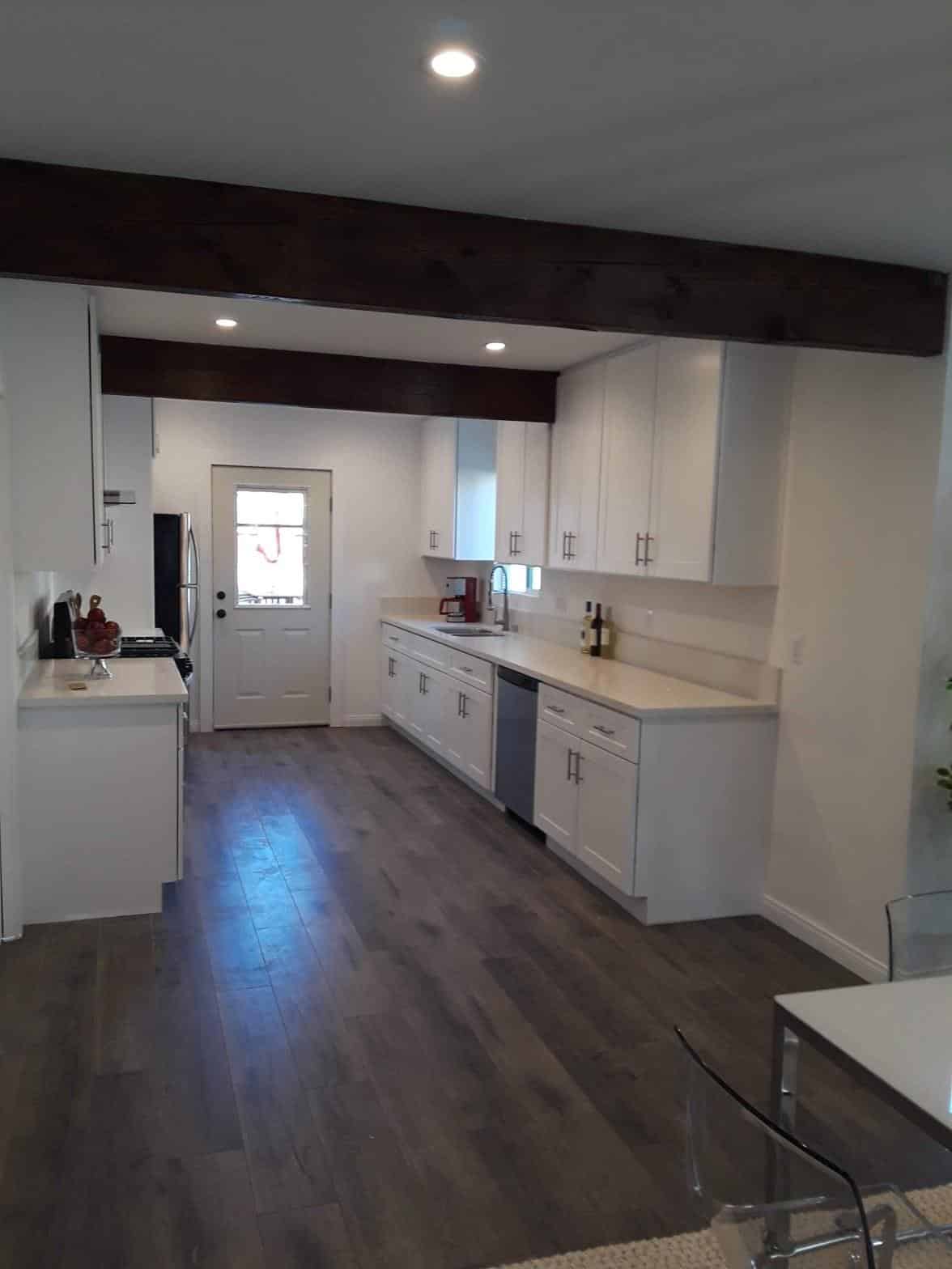 Renovated galley kitchen with white shaker cabinets, dark hardwood floors, and exposed wood ceiling beams in North Hollywood