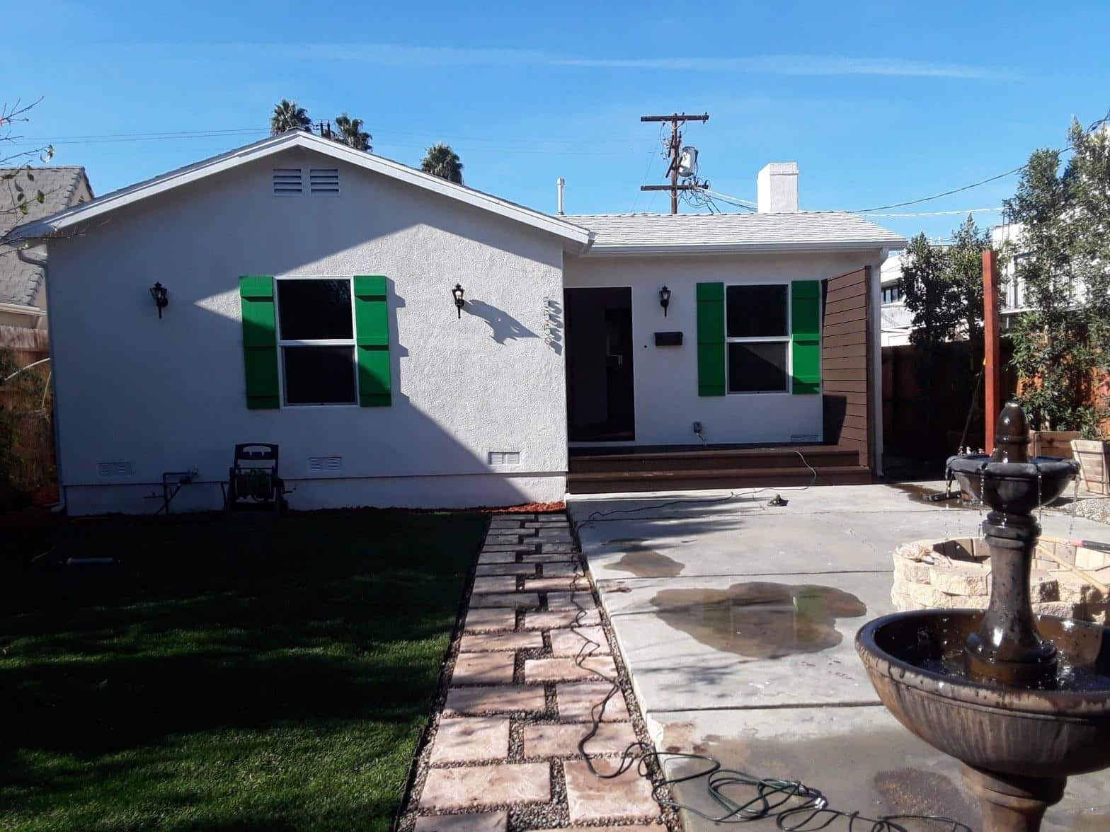 White stucco bungalow with bold green shutters, stone walkway, and decorative fountain after exterior renovation in North Hollywood