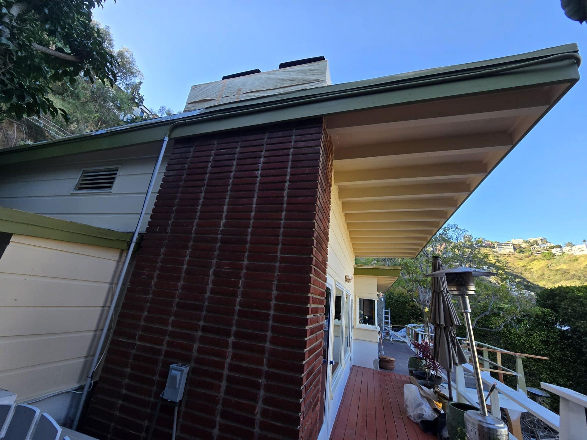 Brick chimney, green roof edge, wood deck, yellow siding exterior | Hollywood Contractor Corp Brick chimney, green roof edge, wood deck, yellow siding exterior — Hollywood Contractor Corp