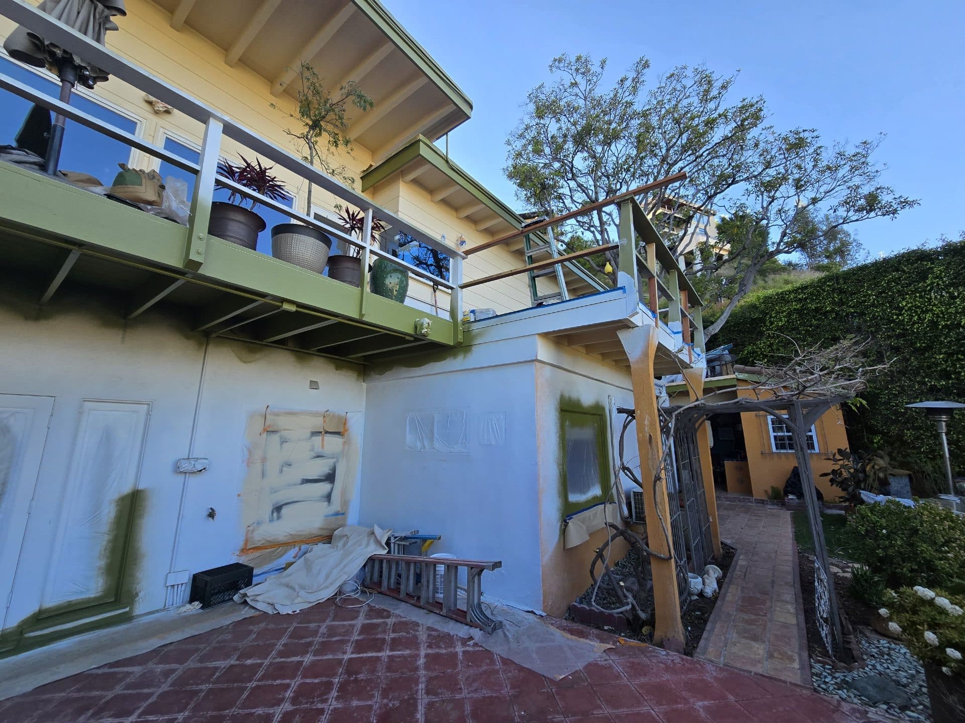 Exterior stucco wall mid-paint, green trim balcony, drop cloths, ladder | Hollywood Contractor Corp Exterior stucco wall mid-paint, green trim balcony, drop cloths, ladder — Hollywood Contractor Corp