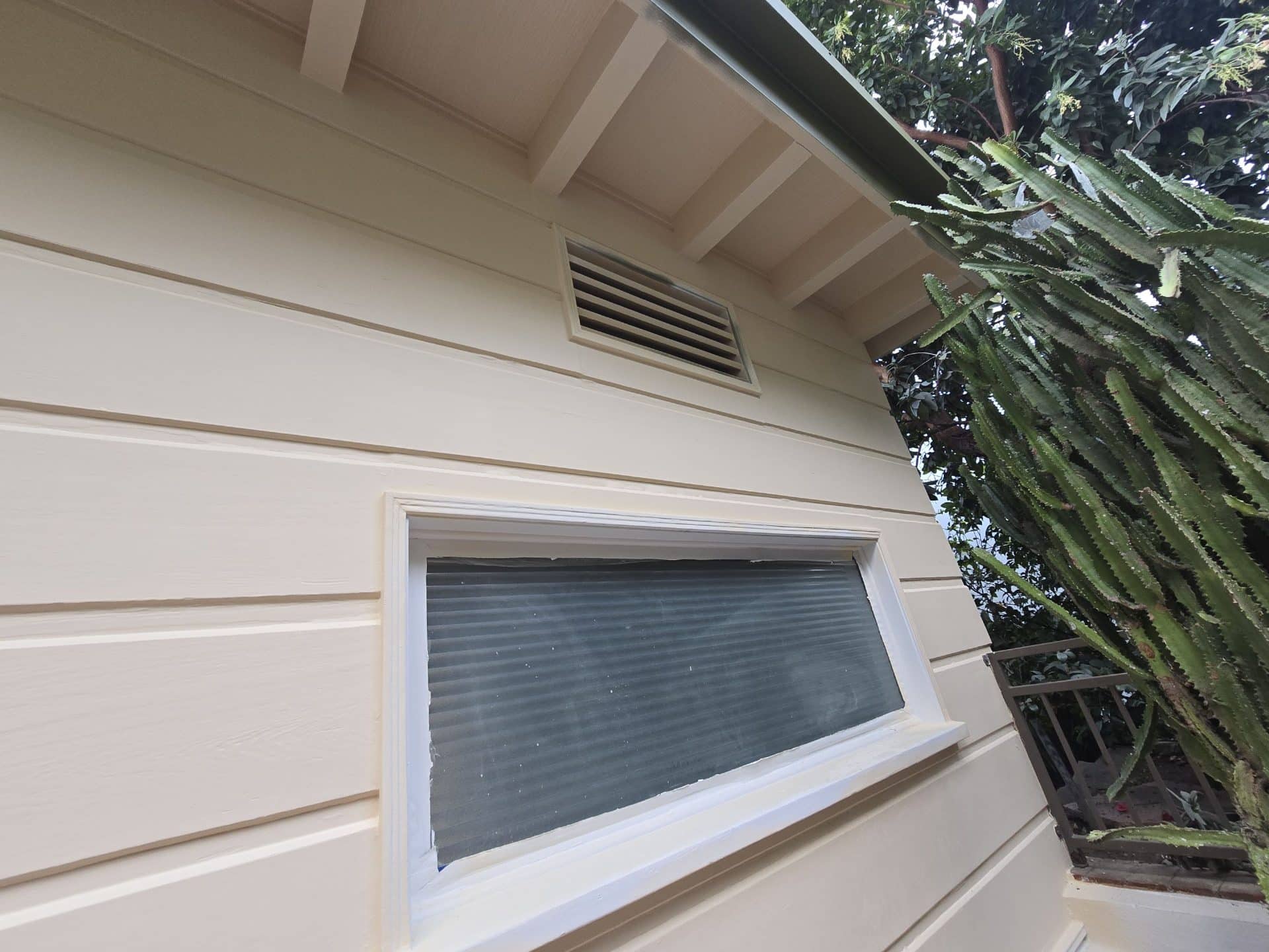 Cream lap siding, white-trimmed transom window, louvered vent, cactus — Hollywood Contractor Corp