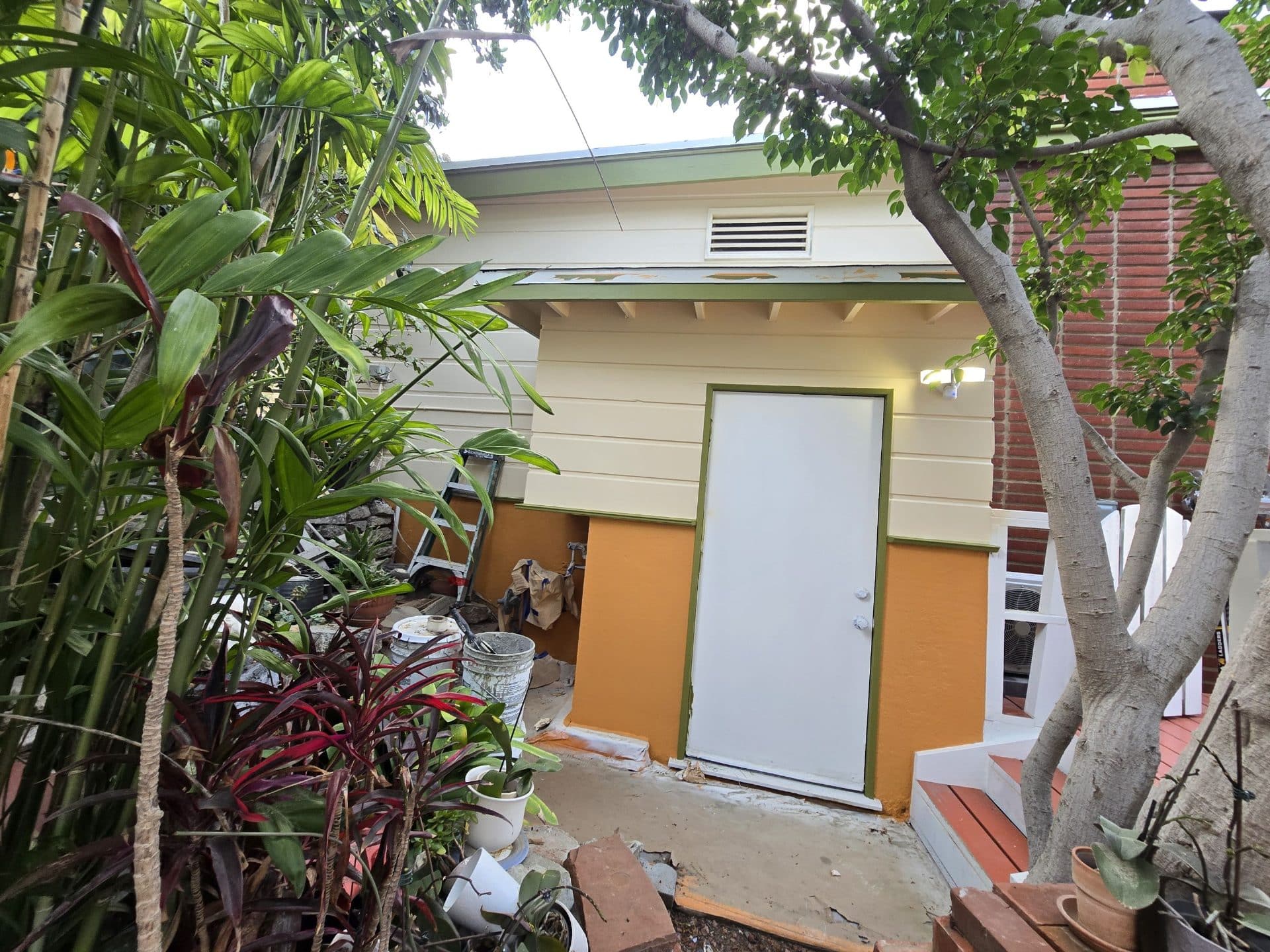 Small outbuilding with new siding, green-trimmed door, and construction debris | Hollywood Contractor Corp Small outbuilding with new siding, green-trimmed door, and construction debris — Hollywood Contractor Corp